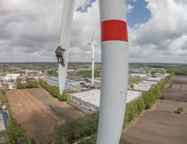 Industriekletterer mit Helm bei der Rotorblattinspektion an einer Onshore-Windenergieanlage